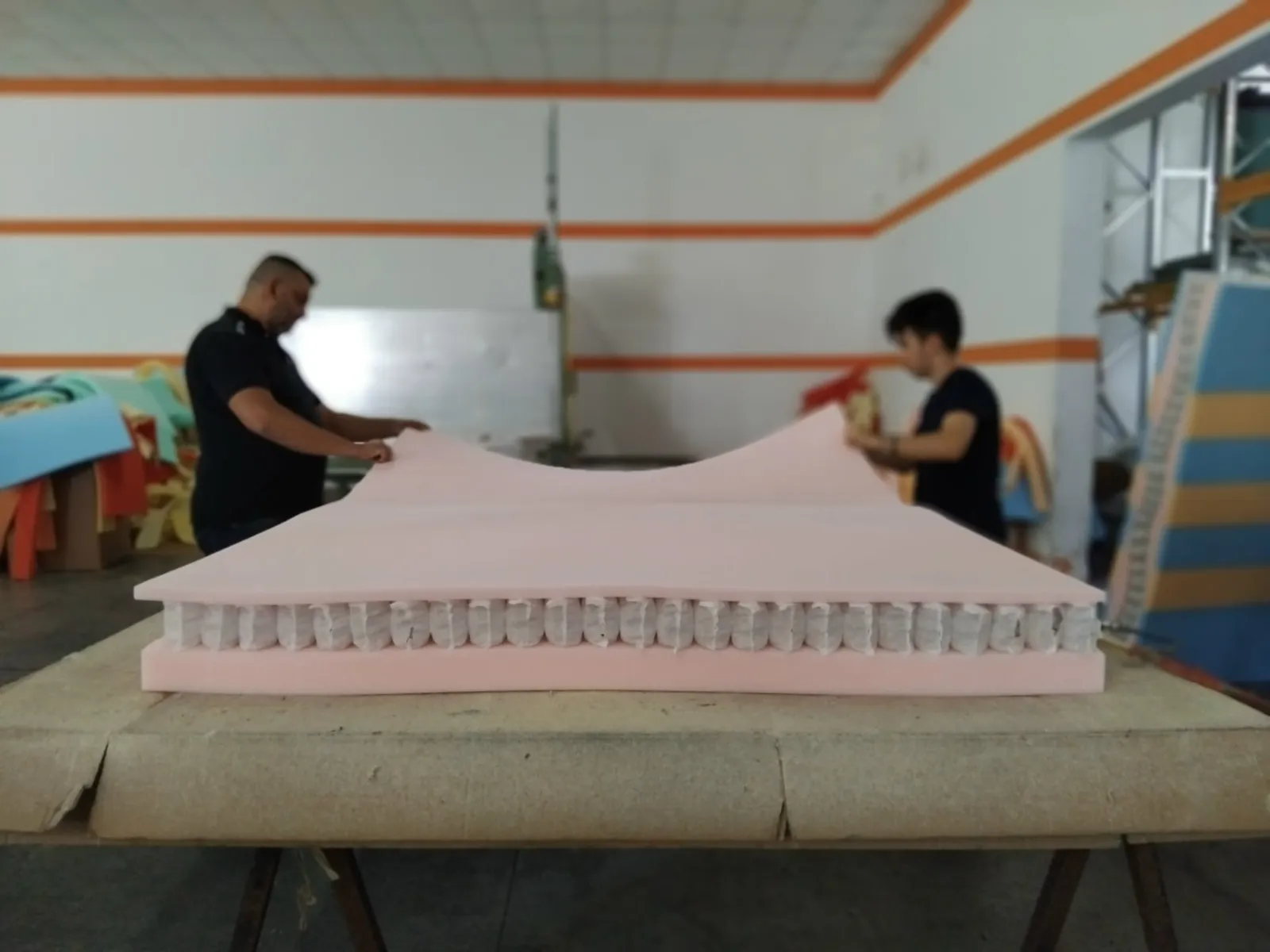 Due operai Secilflex sollevano uno strato di materiale sopra le molle di un materasso, nello stabilimento di Civitaquana